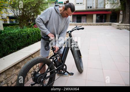 Cycliste jeune homme caucasien ajustant un siège sur vélo électrique, vélo avant de monter. Louer un vélo électrique comme transport urbain écologique. Les gens. A Banque D'Images