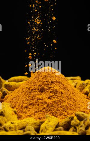 Poudre de curcuma saupoudrée sur la racine de curcuma sèche. Banque D'Images