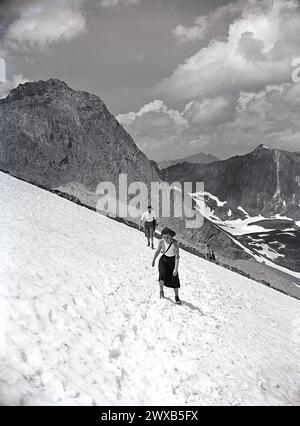 Années 1950, historique, deux dames en jupes marchant sur la neige à flanc de montagne dans les Alpes suisses. Banque D'Images