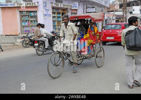 Un pousse-pousse à vélo transporte des passagers dans une rue animée dans une ville, Jaipur, Rajasthan, Inde Banque D'Images