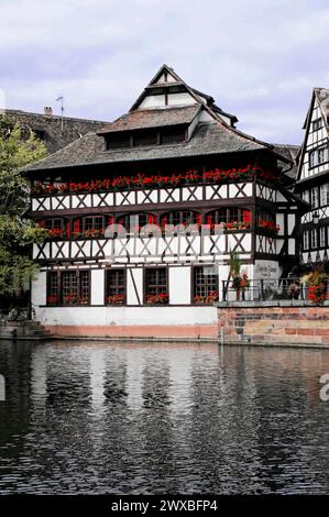 Balade en bateau sur L'ILL, Strasbourg, Alsace, Une maison historique à colombages au bord d'une rivière, décorée de fleurs rouges aux fenêtres Banque D'Images