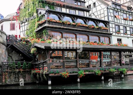 Balade en bateau sur L'ILL, Strasbourg, Alsace, Un restaurant traditionnel aux maisons à colombages et une terrasse fleurie au bord de l'eau Banque D'Images