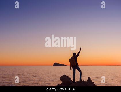 Silhouette de jeune femme randonnée sur la plage rocheuse en Espagne, Benidorm. Regarder la mer agitée et la baie. voyageur appréciant la liberté dans le coucher de soleil serein la Banque D'Images