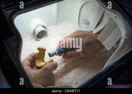 Un technicien dentaire se prépare à polir les détails d'un modèle de pierre dentaire avec la pièce à main pour le rendre prêt à travailler. Banque D'Images