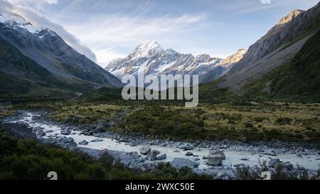 Vallée alpine pittoresque avec rivière glaciaire qui coule à travers et pic proéminent en toile de fond pendant le coucher du soleil. Banque D'Images