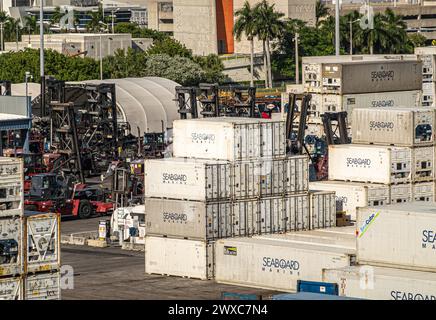 Miami, Floride, États-Unis - 29 juillet 2023 : gros plan, piles de conteneurs Seaboard blanches et machines de transport. Du feuillage vert entre les deux Banque D'Images