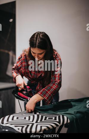 Femme en chemise à carreaux repassage des vêtements sur une planche moderne à la maison. Banque D'Images