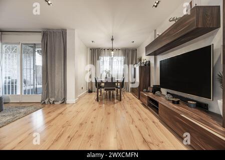 Salon avec table à manger en bois en arrière-plan avec chaises en métal et grande bibliothèque en bois de style moderne avec télévision à écran plat sur le mur Banque D'Images