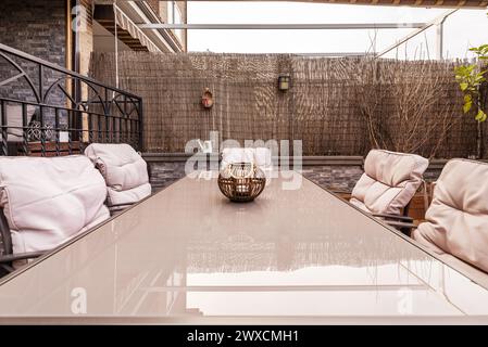 Une table à manger en métal et verre sur une terrasse remplie de plantes avec des meubles en métal lisse et des séparateurs en canne pour plus d'intimité Banque D'Images