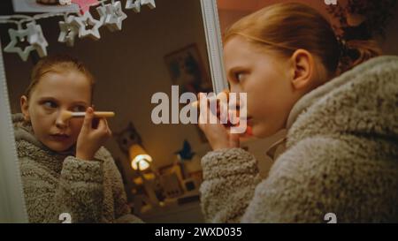 Jeune belle fille fait le maquillage des sourcils debout devant le miroir dans une chambre confortable et confortable. Adolescent caucasien passant du temps libre et s'amusant à la maison dans la soirée. Concept de style de vie Banque D'Images