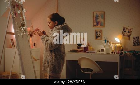 Jeune fille caucasienne fait le maquillage des sourcils debout et regardant dans le miroir dans une chambre confortable et confortable. Adolescente passant du temps libre et s'amusant à la maison la nuit. Concept de style de vie. Banque D'Images