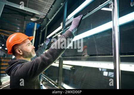 L'homme effectue le pressage d'une fenêtre à double vitrage dans la production de fenêtres Banque D'Images