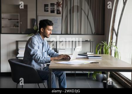 Sérieux et concentré jeune chef de projet indien homme tapant sur ordinateur portable Banque D'Images
