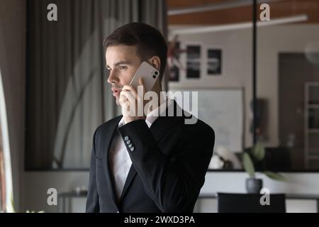 Concentré jeune homme de direction occupé parlant sur téléphone portable dans le bureau Banque D'Images