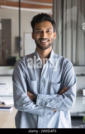 Joyeux bel homme d'affaires indien debout dans le bureau avec les mains pliées Banque D'Images