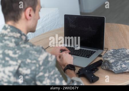 Jeune soldat de l'armée hispanique utilisant un ordinateur portable assis sur une table à la maison Banque D'Images