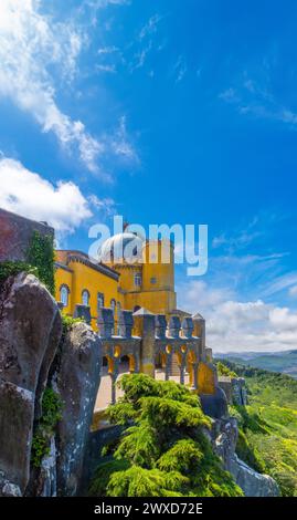 Vue extérieure de la cour voûtée du palais de Pena, peinte en jaune, perchée sur de grands rochers avec la chaîne de montagnes de Sintra en arrière-plan UEDN Banque D'Images