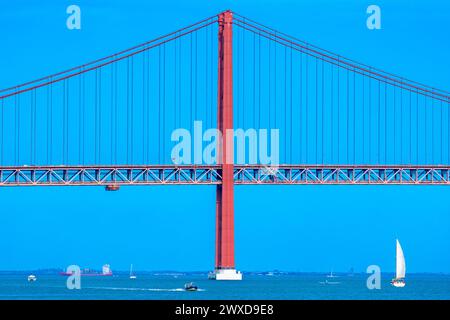 Porte-conteneurs, bateaux à moteur et voiliers naviguant sur le Tage traversant le pont suspendu en acier rouge 25 de Abril avec trafic routier pour l'accès Banque D'Images