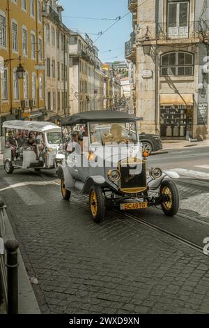 Touristes et familles prenant des photos à l'intérieur d'une réplique d'une vieille voiture de tourisme électrique et d'un véhicule à trois roues grimpant une pente sur un l pavé Banque D'Images