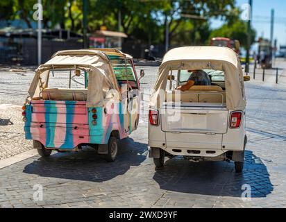 Deux Piaggio APE Calessino 200 Tuk touriste à trois roues garés sur une rue pavée de Lisbonne au Portugal avec des voies de tramway au sol. Banque D'Images