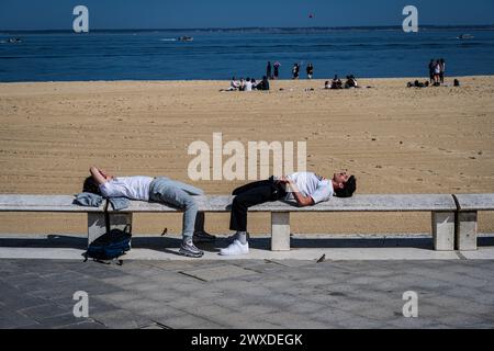 Arcachon, France — 22 mars 2024. Deux jeunes hommes se détendent au soleil sur la plage d'Arcachon, France. Banque D'Images