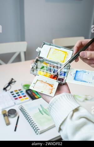 Détail d'un kit de terrain aquarelle. une main d'une femme ramasse un pigment à peindre. Créativité et couleur Banque D'Images