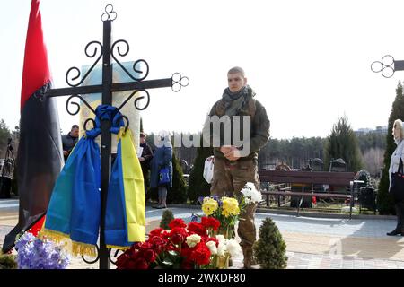 Non exclusif : IRPIN, UKRAINE - 28 MARS 2024 - Un militaire se tient sur la tombe d'un défenseur péri de l'Ukraine au cimetière de la ville d'Irpin sur le Banque D'Images