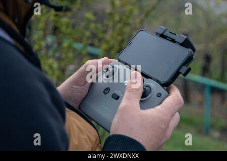 L'homme tient le contrôleur DJI, les pouces sur les bâtons. Panneau de commande gris Drone avec iPhone attaché gros plan à l'extérieur. Vidéographie aérienne, quadcopter. Almaty, Kazakhstan - 19 avril 2023. Banque D'Images