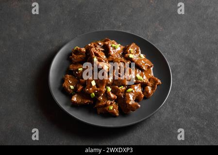 Bœuf de style asiatique avec sauce soja, oignon vert et graines de sésame sur assiette sur fond de pierre sombre. Vue rapprochée Banque D'Images