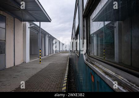 Un train est garé dans une gare avec une passerelle en briques. Le train est bleu et a des fenêtres. La station est vide et le ciel est nuageux Banque D'Images