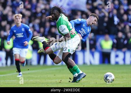 Rocky Bushiri d'Hibernian (à gauche) et Tom Lawrence des Rangers se battent pour le ballon lors du match Cinch Premiership à l'Ibrox Stadium, Glasgow. Date de la photo : samedi 30 mars 2024. Banque D'Images