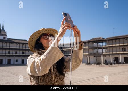 voyageuse d'âge moyen en gilet prenant une photo de la place historique. Sur la Plaza Mayor de Tembleque, à Tolède, dans la déroute Don Quichotte à Castilla L. Banque D'Images