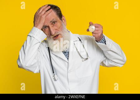 Homme cardiologue médecin mature avec l'anxiété vérifiant le temps sur la montre de poche, courant en retard au travail étant dans la date limite de retard. Pharmacie vieux grand-père inquiétant d'être ponctuel isolé sur fond jaune Banque D'Images