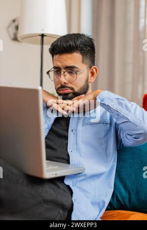 Bouleversé jeune homme indien allongé sur le canapé à la maison en utilisant un ordinateur portable ayant l'anxiété et le stress. Un homme hispanique barbu choqué réagissant à la perte, de mauvaises nouvelles sur netbook dans l'appartement du salon. Virus informatique. Banque D'Images