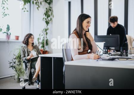 Cadre de bureau contemporain avec femme souriante travaillant au bureau, collègues en arrière-plan Banque D'Images