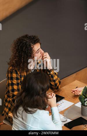 Femme d'affaires réfléchie dans la réunion discutant de la stratégie du projet avec des collègues réunis à table. Banque D'Images