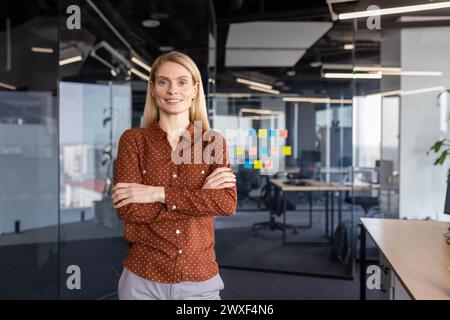 Portrait de femme d'affaires heureuse et réussie, patron en chemise souriant et regardant la caméra à l'intérieur du bureau avec les bras croisés. Femme d'affaires expérimentée mature sur le lieu de travail, employé de l'entreprise. Banque D'Images