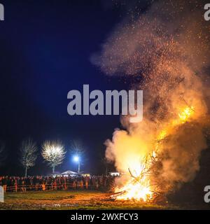 Sythen, NRW, Allemagne. 30 mars 2024. Les habitants et les visiteurs se rassemblent pour le feu de joie annuel de Pâques à la ferme Prickingshof à Sythen, Westfalie (Münsterland). L'allumage des feux de joie de Pâques est une tradition depuis de nombreux siècles en Allemagne, généralement le samedi Saint ou le dimanche de Pâques. Les services d’incendie et d’urgence veillent à ce que le feu soit protégé pendant que les bénévoles ont soigneusement inspecté le bois de chauffage pour s’assurer qu’aucune faune ne s’est réfugiée dans les branches. Crédit : Imageplotter/Alamy Live News Banque D'Images