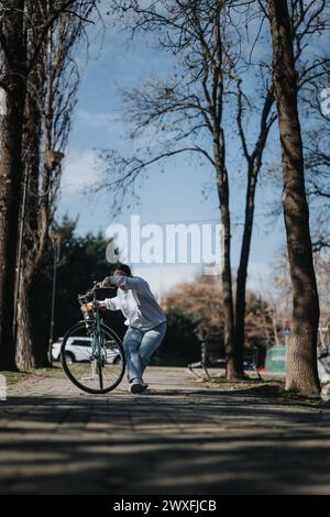 Femme active poussant sa bicyclette le long d'un chemin bordé d'arbres dans le parc. Banque D'Images