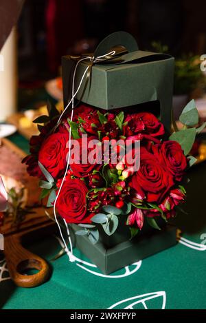 Un superbe arrangement de roses rouges et de verdure présenté dans un élégant coffret cadeau vert foncé avec un ruban doré. Banque D'Images
