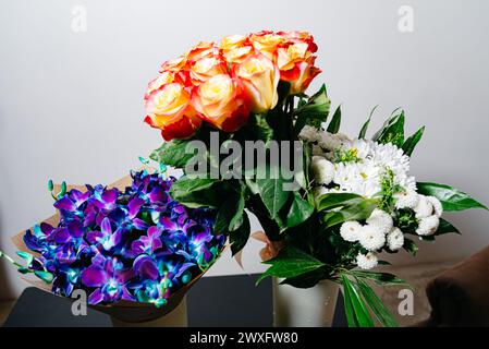 Trois bouquets variés : roses orange-jaune éclatantes, orchidées bleues frappantes, et un arrangement classique de marguerites blanches, chacun présentant une beauté unique. Banque D'Images