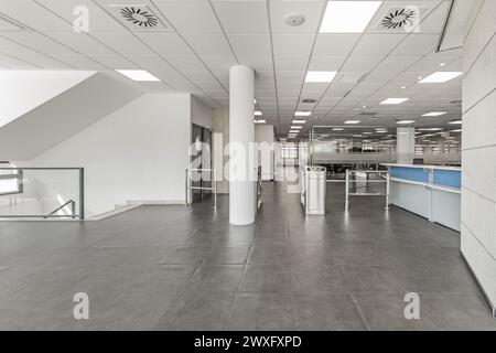 Espace d'accès aux bureaux avec bureau d'accueil, plafonds techniques, sols gris et bureaux dans des aquariums en verre Banque D'Images