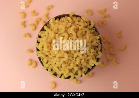 Vue de dessus crue séchée coude Macaroni pour la cuisson des pâtes, sur bol en céramique Banque D'Images