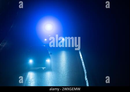SYMBOLE - 29 mars 2024, Rhénanie-Palatinat, Nürburg : une voiture de police roule derrière un véhicule sur une route dans l'obscurité avec des feux bleus clignotants sur le "vendredi voiture" au Nürburgring. Car Friday' est l'ouverture de la saison pour les fans de voitures. Photo : Silas Stein/dpa Banque D'Images