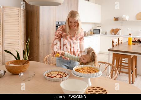 Heureuse mère avec sa petite fille pressant du citron sur une tarte aux pommes crue dans la cuisine Banque D'Images