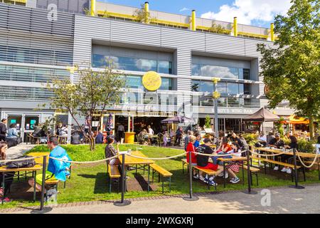 Les gens mangent à l'extérieur dans les restaurants de Here East le long du canal de navigation de la rivière Lee, Olympic Park, Stratford, Londres, Angleterre Banque D'Images