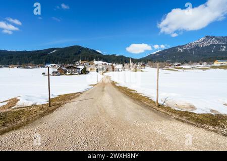 Un village alpin enneigé avec un chemin de terre coupant le paysage Banque D'Images