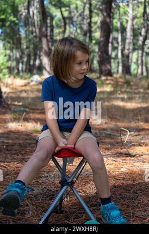 Garçon blond assis sur une chaise dans les bois Banque D'Images