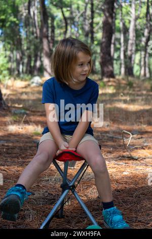 Garçon blond assis sur une chaise dans les bois Banque D'Images