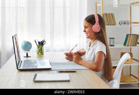 Bonne écolière preteen dans les écouteurs étudiant en ligne à la classe virtuelle avec le tuteur de professeur. Banque D'Images